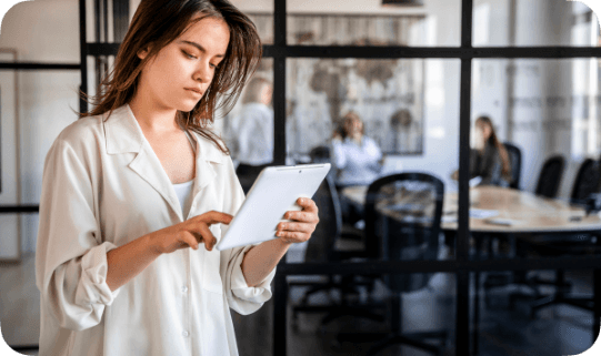 Professional using a tablet to review inspection data in a modern office environment, with team members collaborating in the background.