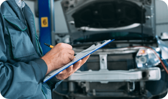 Vehicle inspector taking notes on a clipboard while checking a car with the hood open
