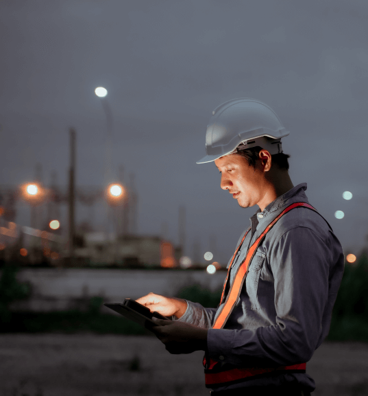 Field technician wearing a hard hat uses a tablet at an oil and gas facility during an on-site inspection, supported by Quality Management Software for Oil & Gas Operations.